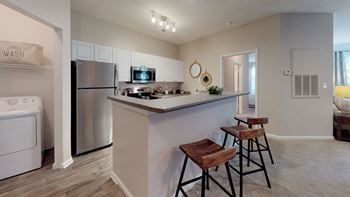 A kitchen with a breakfast bar and stools next to a washer and dryer